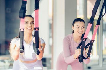 Athlete woman doing push ups with trx fitness straps, laughing in the gym while join lessons in sport club. Workout and healthy lifestyle concept