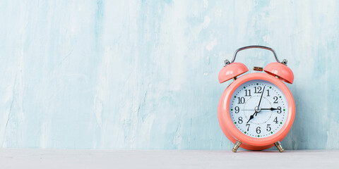 Pink alarm clock on the table, on blue background. Copy space.