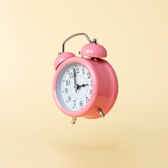 The pink alarm clock is levitate in the air, against a yellow background. The concept of time, copy...
