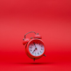 The red alarm clock is levitate in the air, against a red background. The concept of time, copy...