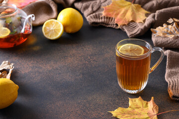 Warming black tea with lemon in cozy lifestyle with fall leaves and cozy scarf on brown background....