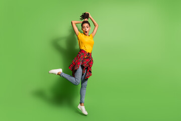 Full length body size view of lovely funky worried girl jumping having fun making hairdo isolated over bright green color background