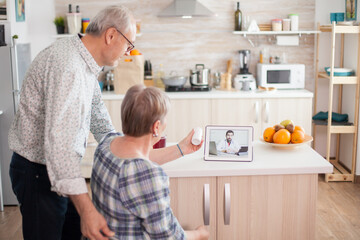 Old couple during online consultation with doctor. Video conference with doctor using laptop in kitchen. Online health consultation for elderly people drugs ilness advice on symptoms, physician