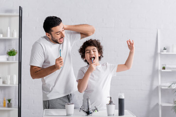 Muslim boy with toothbrush singing near father in bathroom