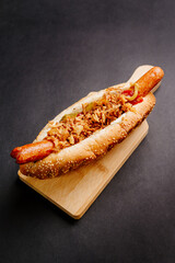 Danish hot dog with fried sausage, ketchup, mustard sauce and raw and fried onions isolated on black background