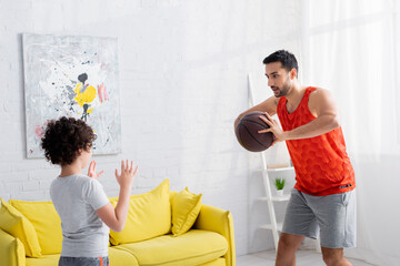 Muslim man playing basketball with son in living room