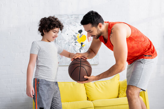 Smiling arabian man with basketball teaching son at home