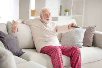 Photo of aged man pensioner sit couch home rest relax look watch tv cinema switch channel remote controller