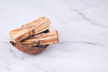 Palo Santo tree sticks inside coconut shell on light marble background - holy incense tree from...