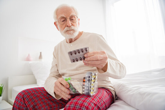 Photo of senior man unhappy sad sit bed look read instruction pills drugs painkiller unhealthy pain ill indoors