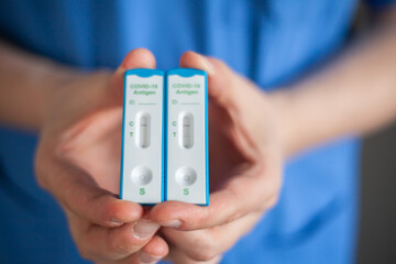 The doctor with stethoscope holds a negative and positive antigen tests Covid-19 in his hands 
