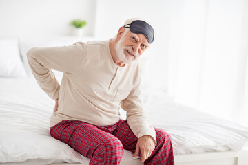 Photo of elderly man sit on bed home unhappy sad upset ache hurt spasm in spine health healthcare medicine