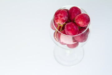 Big red grapes in an empty glass, top view, close-up on a white background