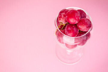 Fototapeta na wymiar Big red grapes in an empty glass, top view, close-up on a pink background