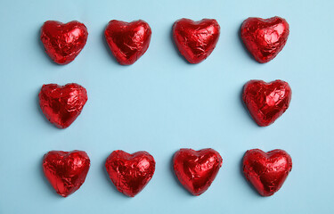 Frame of heart shaped chocolate candies on light blue background, flat lay with space for text. Valentine's day treat