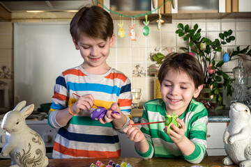 Two little kid boy coloring eggs for Easter holiday in domestic kitchen, indoors. Sibling brothers having fun and celebrating feast