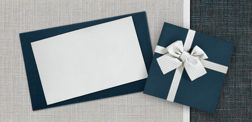 Gift card and gift box with ribbon and bow isolated on elegant blue and grey fabrics background,...