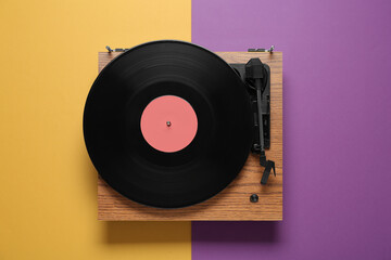 Modern turntable with vinyl record on color background, top view