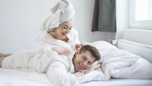 Funny young couple lying together after bathroom, shower, enjoy weekends. Husband and wife in love, laughing, smiling and having fun.