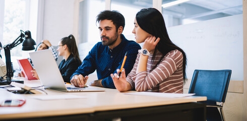 Pensive coworkers sharing laptop while working