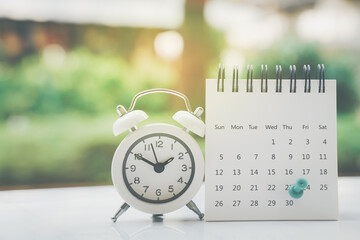 white calendar with green thumbtacks marked the last day of month and white alarm clock on white...