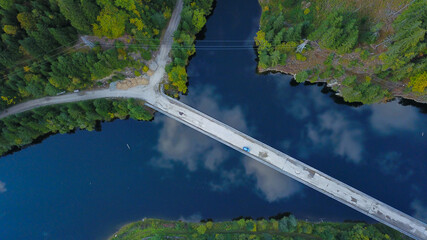 Above view from drone flight of a car crossing a bridge over a lake. The clouds are reflecting into the calm waters of the lake. Carpathia, Romania.