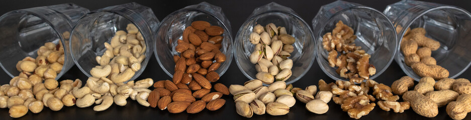 mixture of nuts (peanuts, pistachios, almonds, walnuts, hazelnut, cashew) in glasses with black background