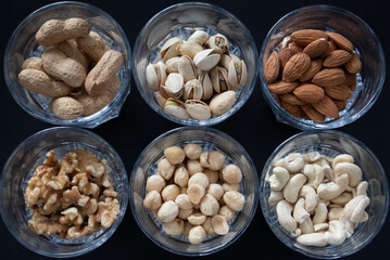mixture of nuts (peanuts, pistachios, almonds, walnuts, hazelnut, cashew) in glasses from top view with black background