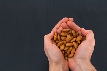 person holding almonds on his hands with black background and copy space