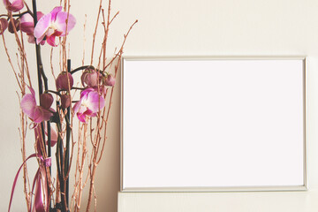 silver horizontal empty frame on white table with pink orchid flowers, mockup for arts, photos illustrations