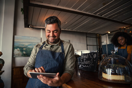 Male waiter browsing on digital tablet scrolling through menu standing against counter in funky cafe 