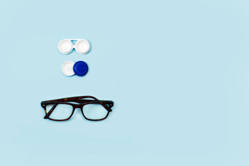 Envase abierto para lentillas junto a un par de gafas sobre un fondo celeste liso y aislado. Vista...