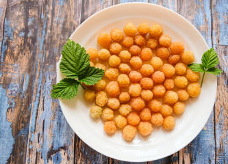 Ripe yellow raspberry lies on a white plate on a blue wooden background.