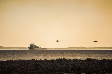 helicopters fly above warship