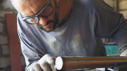 Obraz premium Adult repairman in protective eyewear examining a fixed pipe on table at workshop. Male mechanic preparing to weld metal detail at garage. Concept of maintenance service. Close up Slow motion