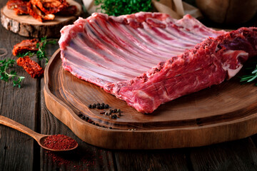 Raw lamb meat on the bone in a large whole piece, organic mutton with seasonings on a wooden...
