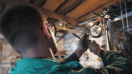 Male mechanic in protective glasses examines vehicle detail in garage. Male worker using tool for his work at workplace. Young repairman in uniform working in workshop. Close up Slow motion