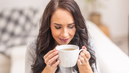 Young brunette woman holding a cup of tea or coffee and smelling lovely aroma