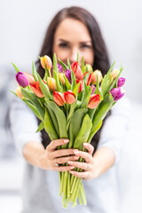 Happy dark haired woman holding in front of her a lovely bouquet full of tulips during national womens day