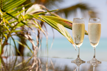 Two glasses of chilled prosecco over tropical background