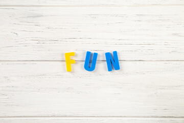 The sign, word fun on a white wooden background, top view. Children colored plastic letters