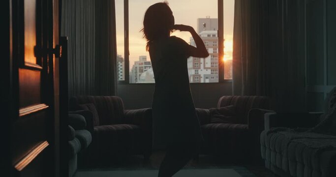 Young woman dances alone near the window and takes off her dress