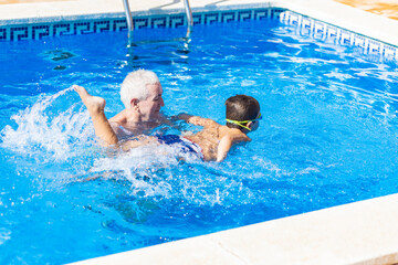 Grandfather teaching his grandson to swim in a pool