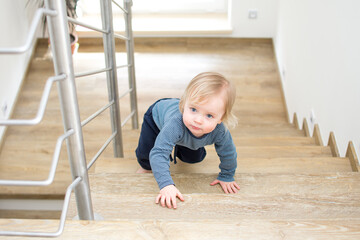 Small caucasian baby crawling on the stairs. Indoor portrait with copy space. Kid danger and safeness at home.