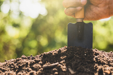 The man's hand was using a shovel to scoop into the loam to plant trees.
