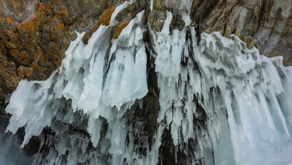 Amazing bizarre icicles hang from the roof of the grotto in the rock. Stone and ice texture.