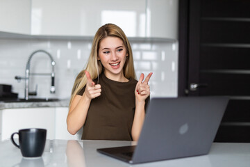 Young woman talking on video call and waving hand while sitting at table in the kitchen