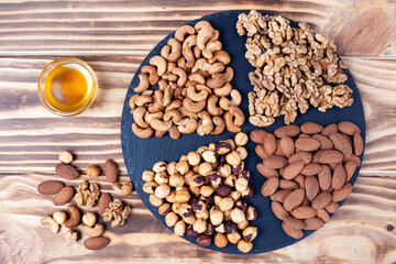 Various nuts sorted in glass bowl with honey bowl and honey dipper