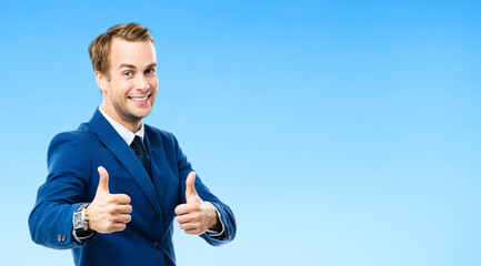 Fototapeta premium Portrait of confident businessman showing thumbs up hand sign gesture, on blue background. Business success concept. Young happy smiling man at studio.