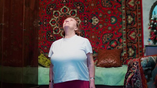 Seniour woman does tibetian gymnastics as morning exercises. Isolation of old people at home during pandemic.